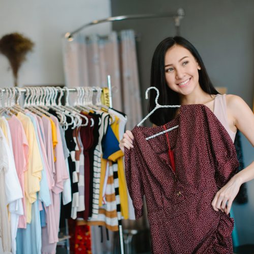 Positive woman choosing new clothes in shop and smiling